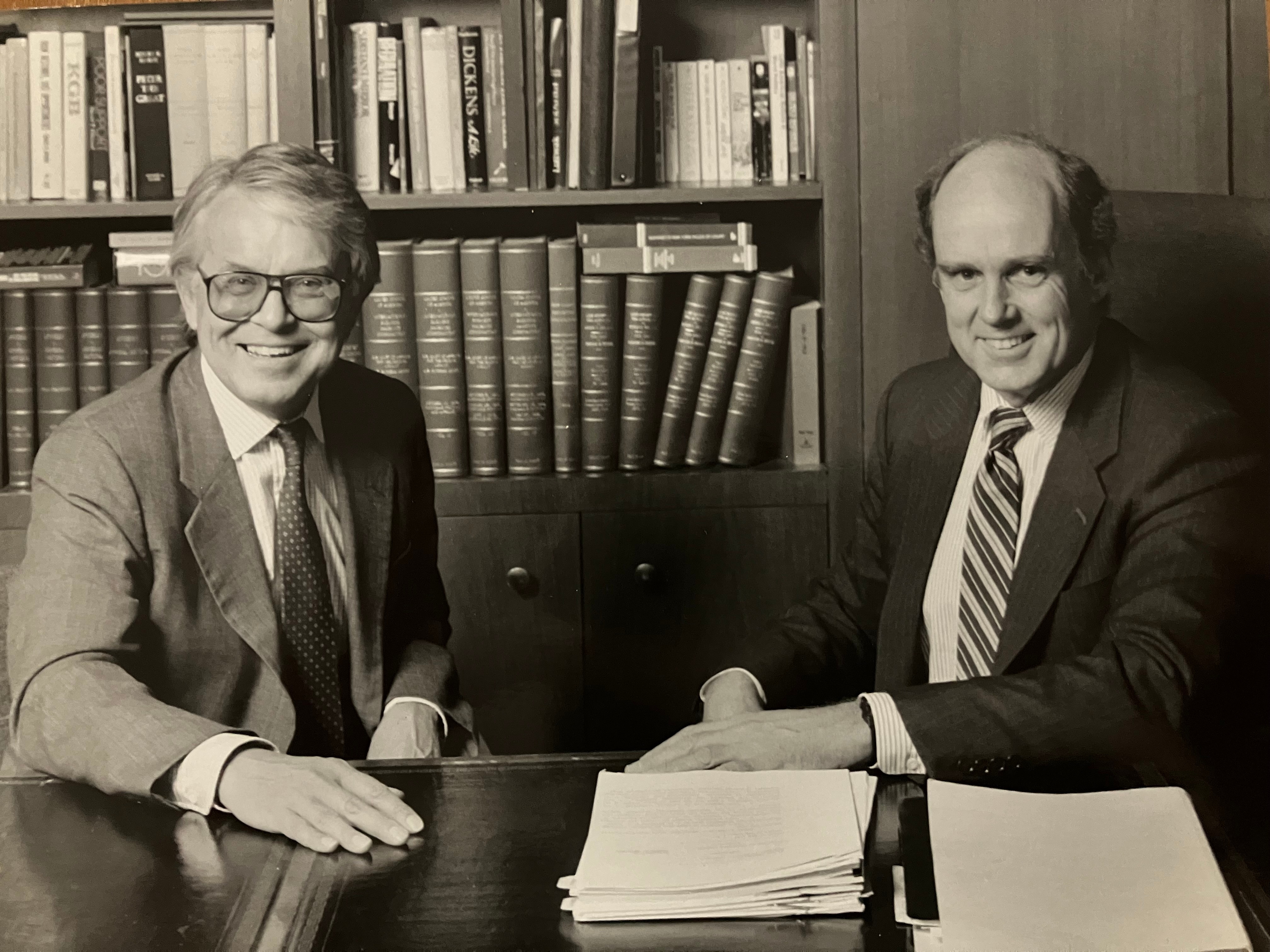 The picture shows Paul sitting with his law partner at a table with thick books in the background.