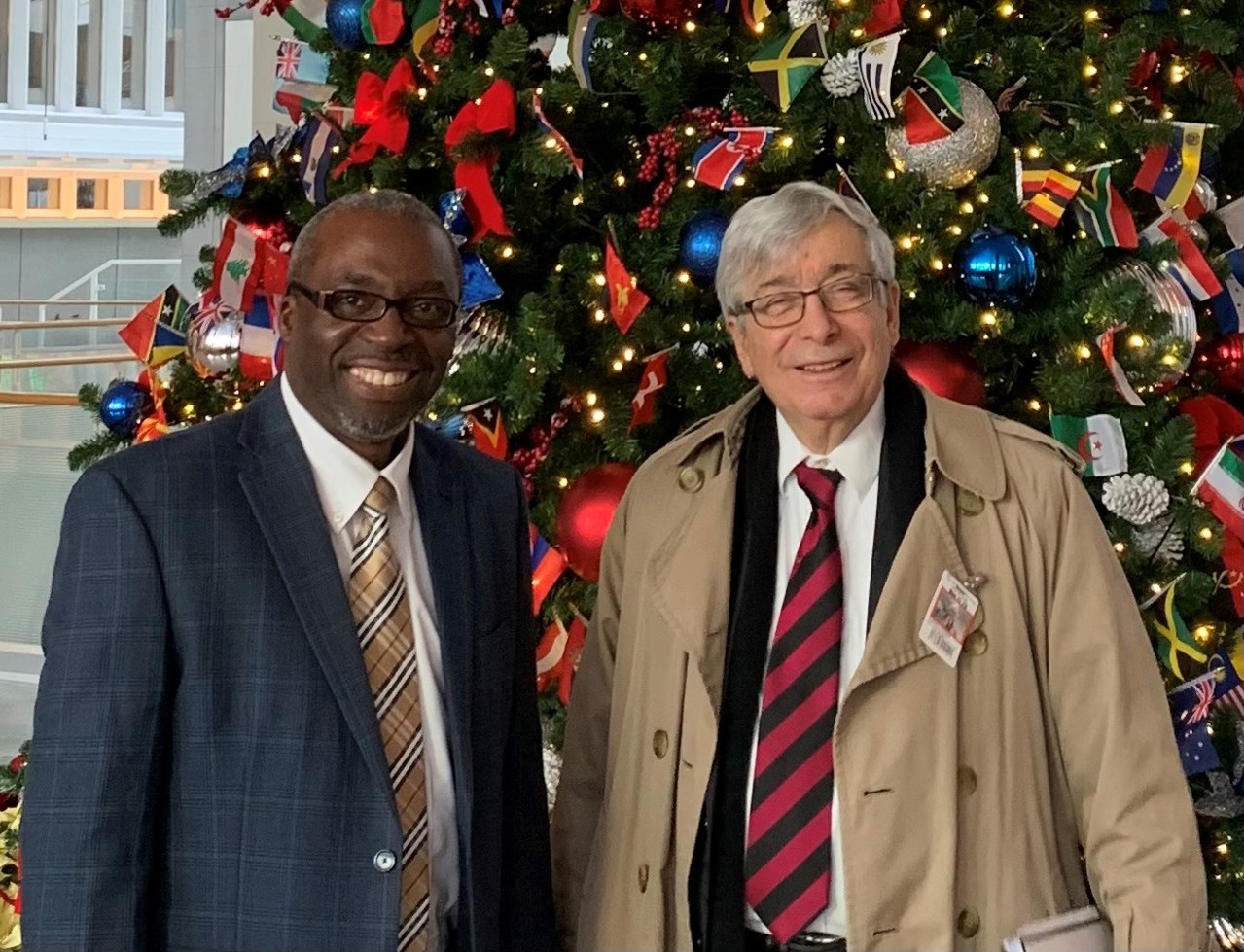 Kenneth to the left and Sir Rick on the right, both smiling in front of a Christmas tree.