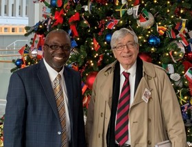 Kenneth to the left and Sir Rick on the right, both smiling in front of a Christmas tree.