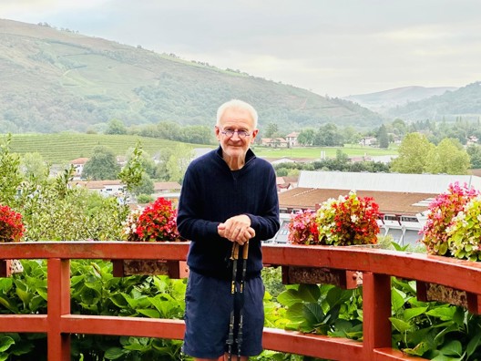 Rob stood overlooking mountains and greenery. He is holding two walking sticks.
