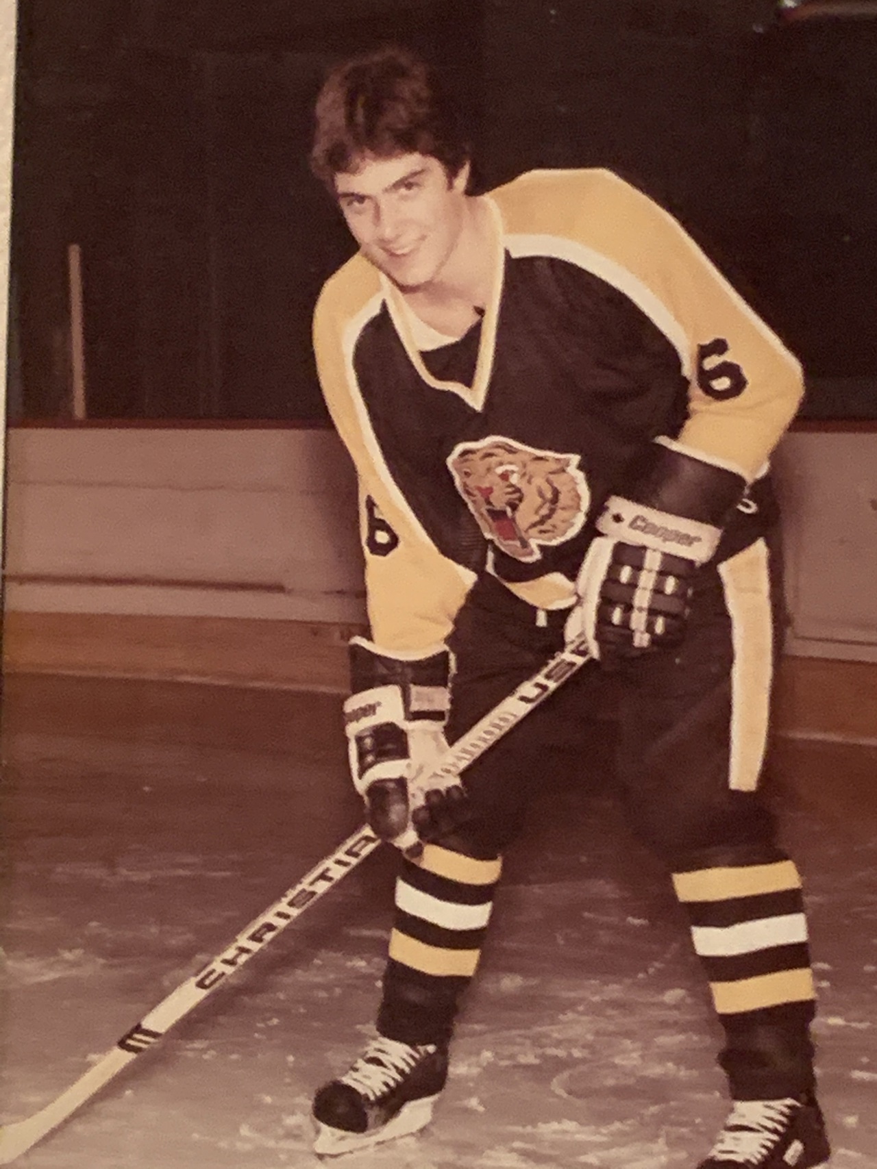 Paul wearing a yellow and navy hockey uniform, he is skating on an ice rink, holding a hocket stick and looking at the camera.