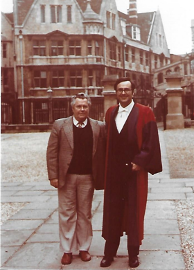 The picture shows Jim in a graduation gown with Hertford College and the Bridge of Sighs in the background. Jim's father is in a suit and is standing next to him.