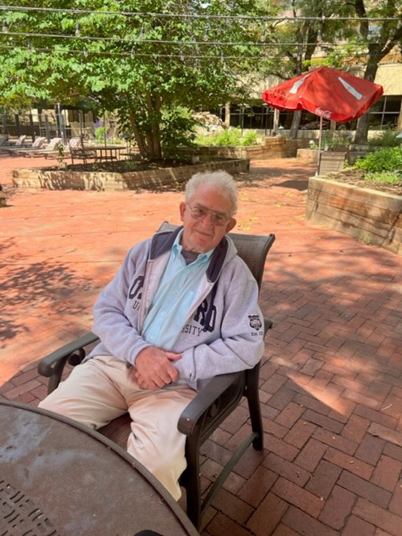 Joe sitting in a chair. He is wearing a sweatshirt over a sky-blue shirt and beige pants.