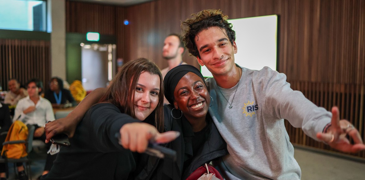 An image of three students with their arms around each other, posing for a photo and smiling. One of the students is wearing a jumper with the Rise logo on it.