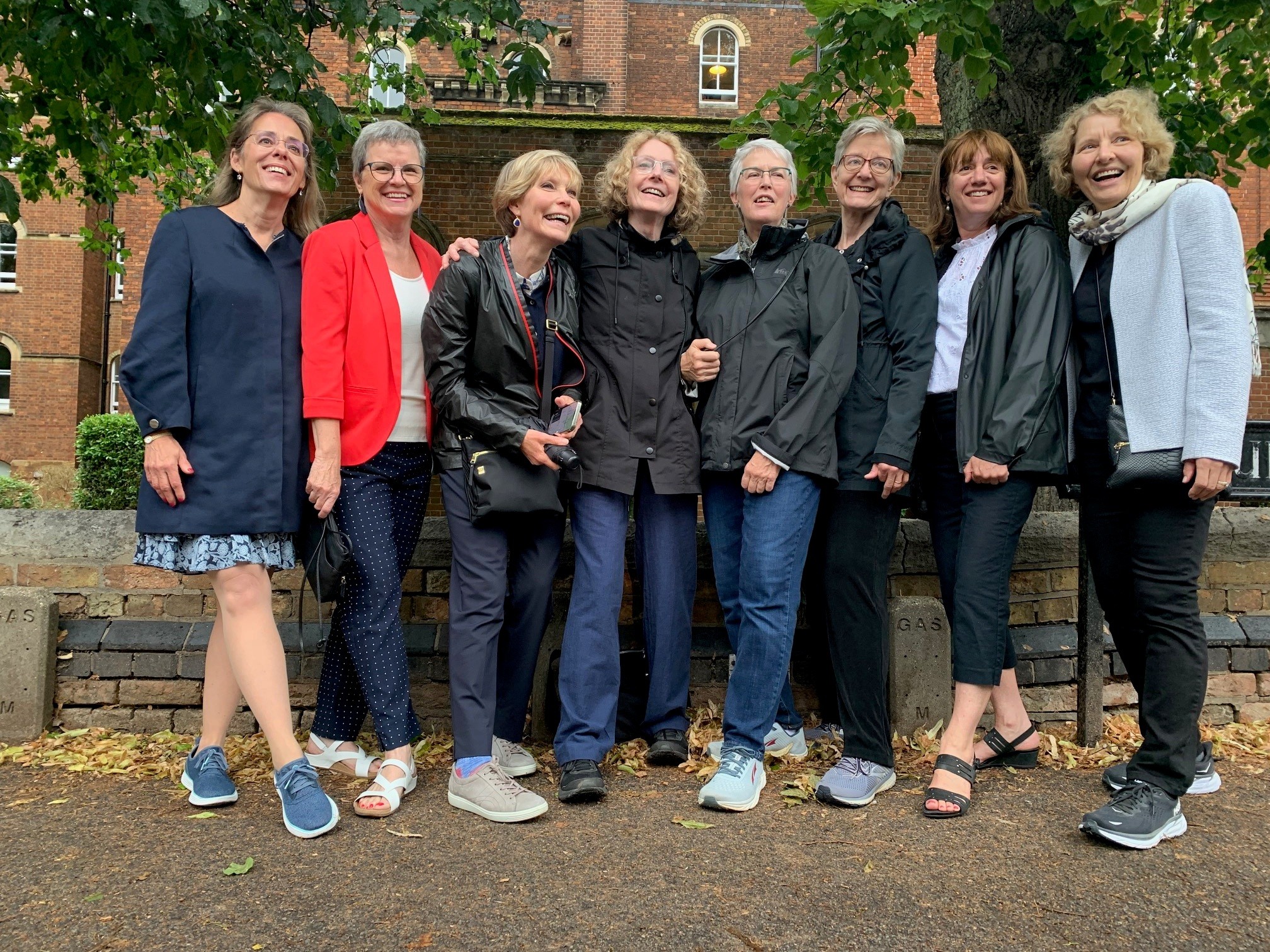 Group of 8 women stood side by side smiling and posing before a brick building.