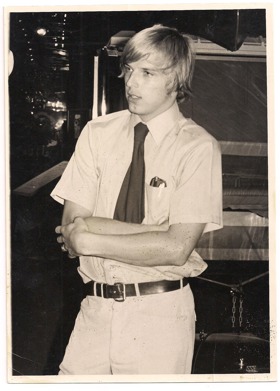 Black and white photo of Geza as a young man, wearing a shirt and tie, leaning with arms crossed.