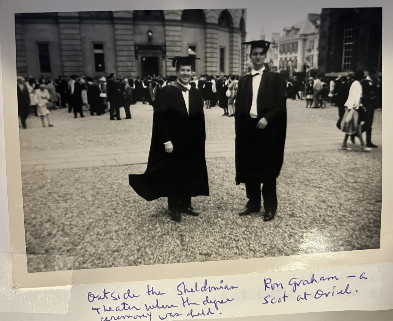 A black-and-white picture of Bob and his Scottish friend Ron Graham of Oriel College dressed in gowns and standing in front of the Sheldonian Theatre with a crowd of similarly-dressed students in the background
