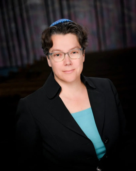 A portrait of Lisa showing her in a black coat and a blue top. She's wearing a kippah.
