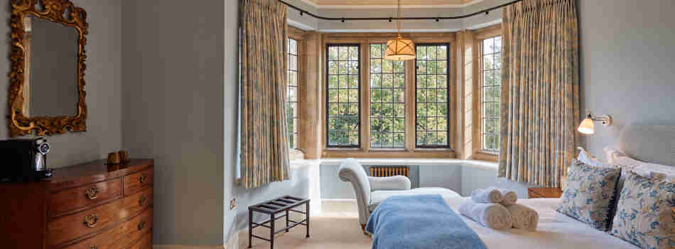 A Bedroom With Blue Walls And Blue Coloured Soft Furnishings Facing The Camera Are Large Old Fashioned Windows That Allow Light To Flood In