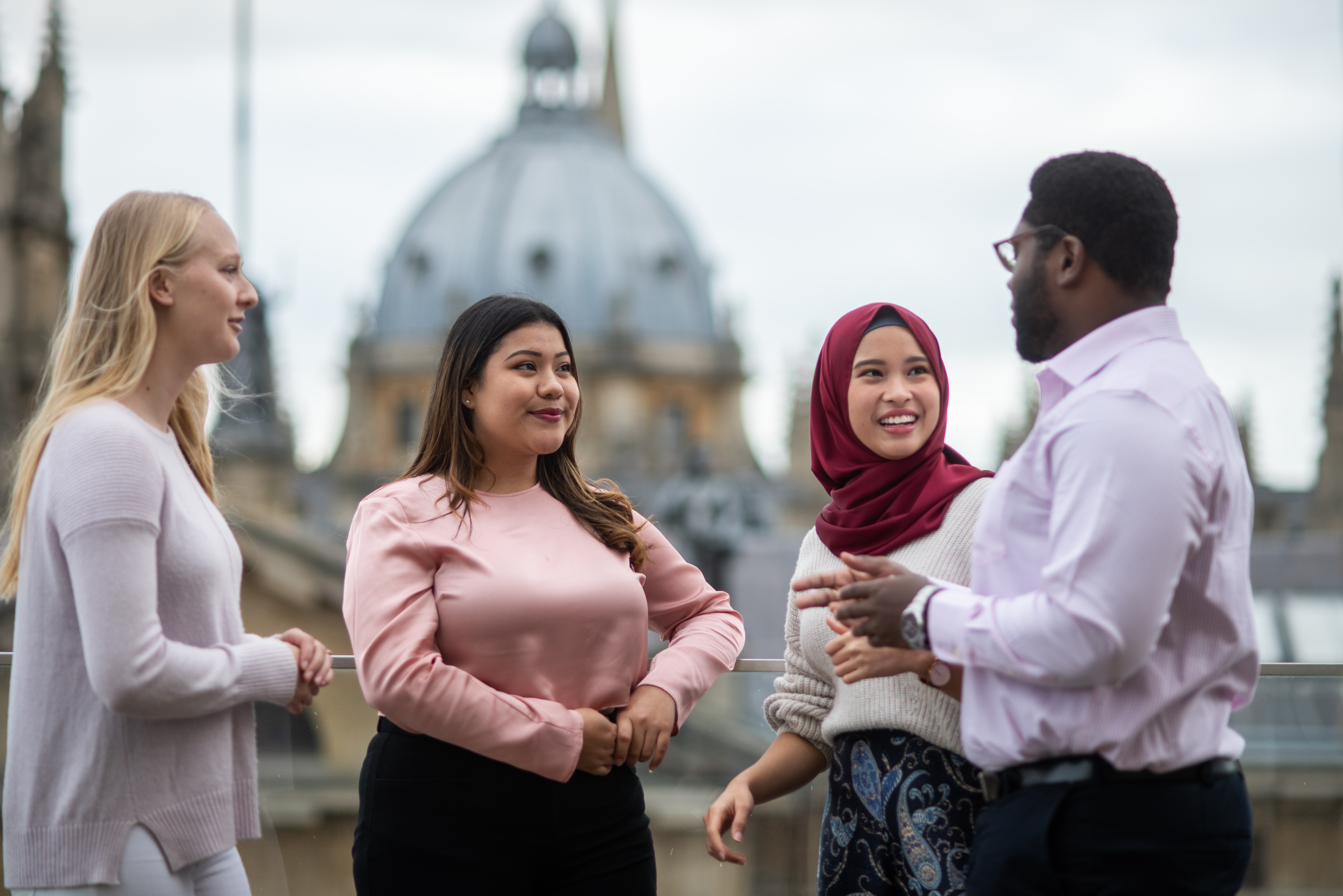 Four Rhodes students talking in a group. In the background is the domed roof of the Rhodes House building.