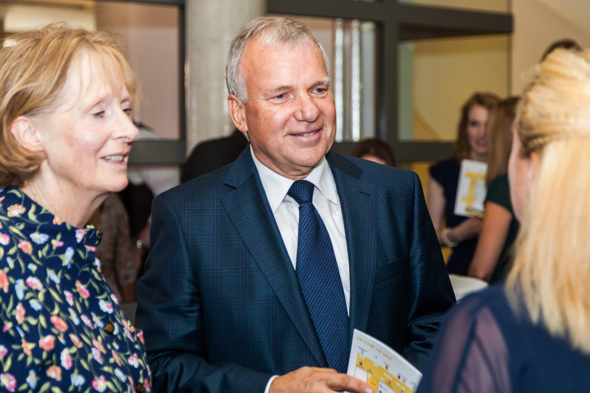 Claus in a suit talking to a woman with her back to the photo, with his wife Clare stood to the left of him.
