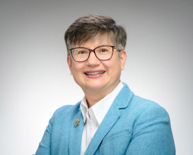 Elisabeth is smiling at the camera, she wears a white shirt and blue blazer, as well as glasses.