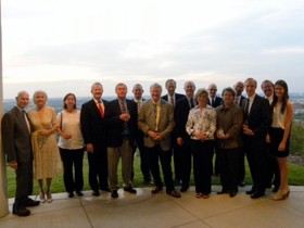 The picture shows a group of people in formal attire standing at the edge of a field.