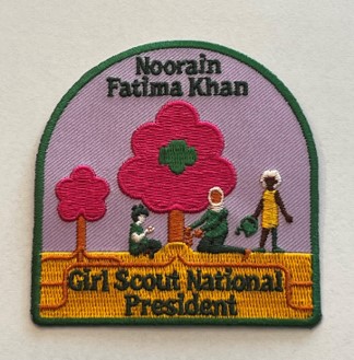 Noorain's embroidered Girl Scout patch, which has a green border, purple background, pink trees and tree people pictured watering the central tree. The top green stitching reads 'Noorain Fatima Khan' and the bottom 'Girl Scout National President'