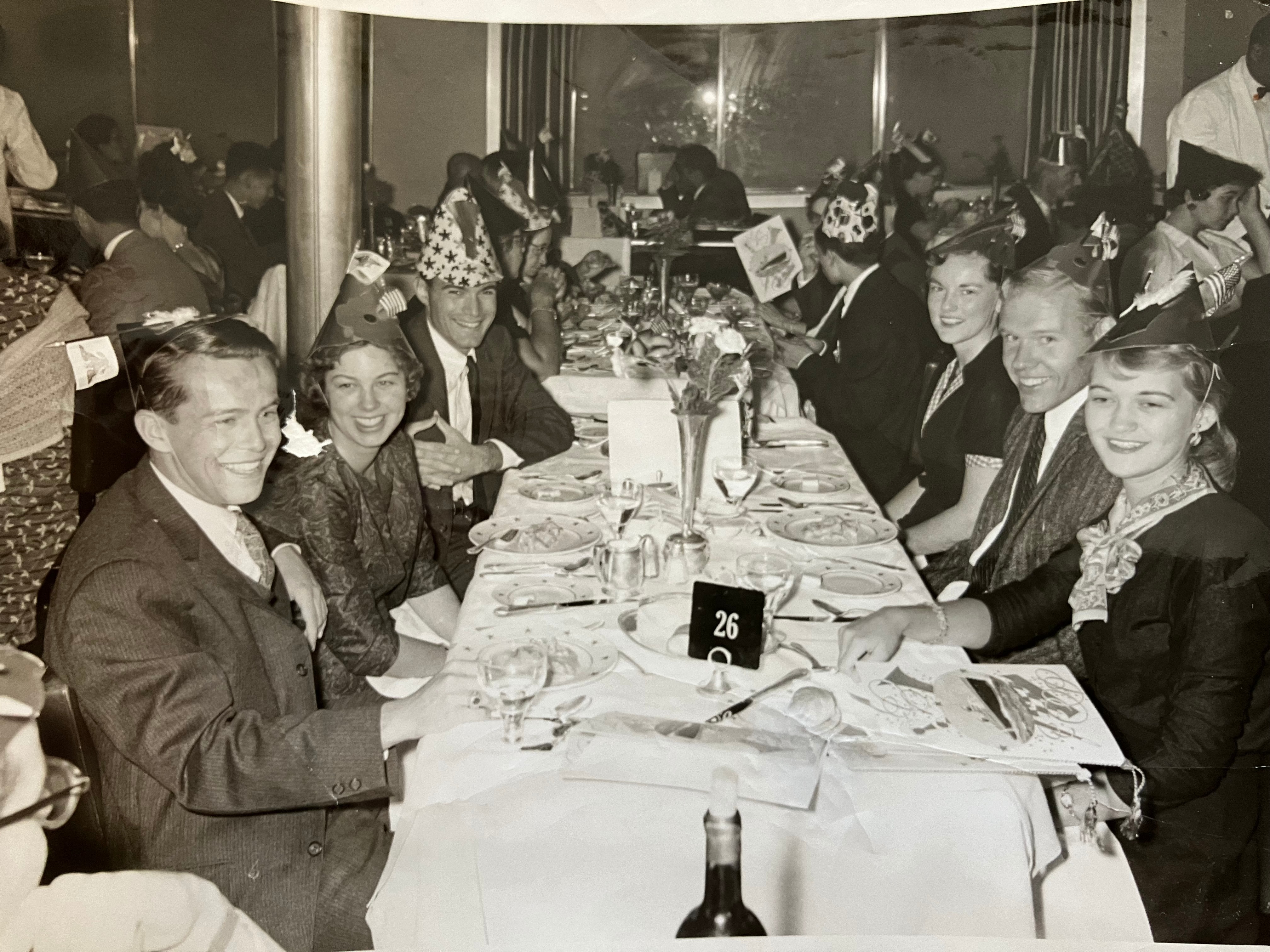 A black-and-white picture showing Paul at a dinner with several other people. The table is laid out with crockery and cutlery.