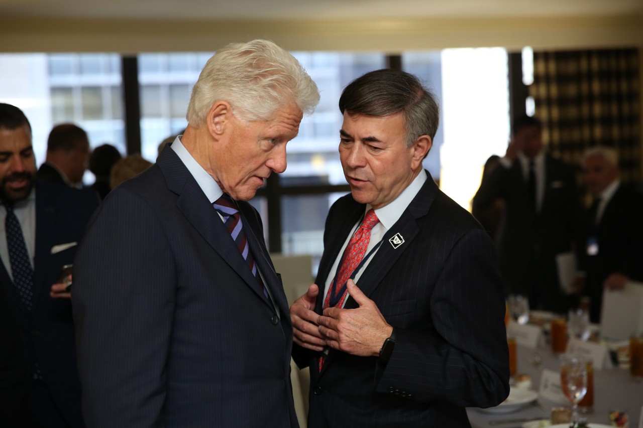 Bob standing to the right of Bill Clinton talking to him, with Bill leaning head down and intently listening.