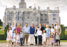 The whole family standing smiling before a castle, with the words 'Merry Christmas' above them