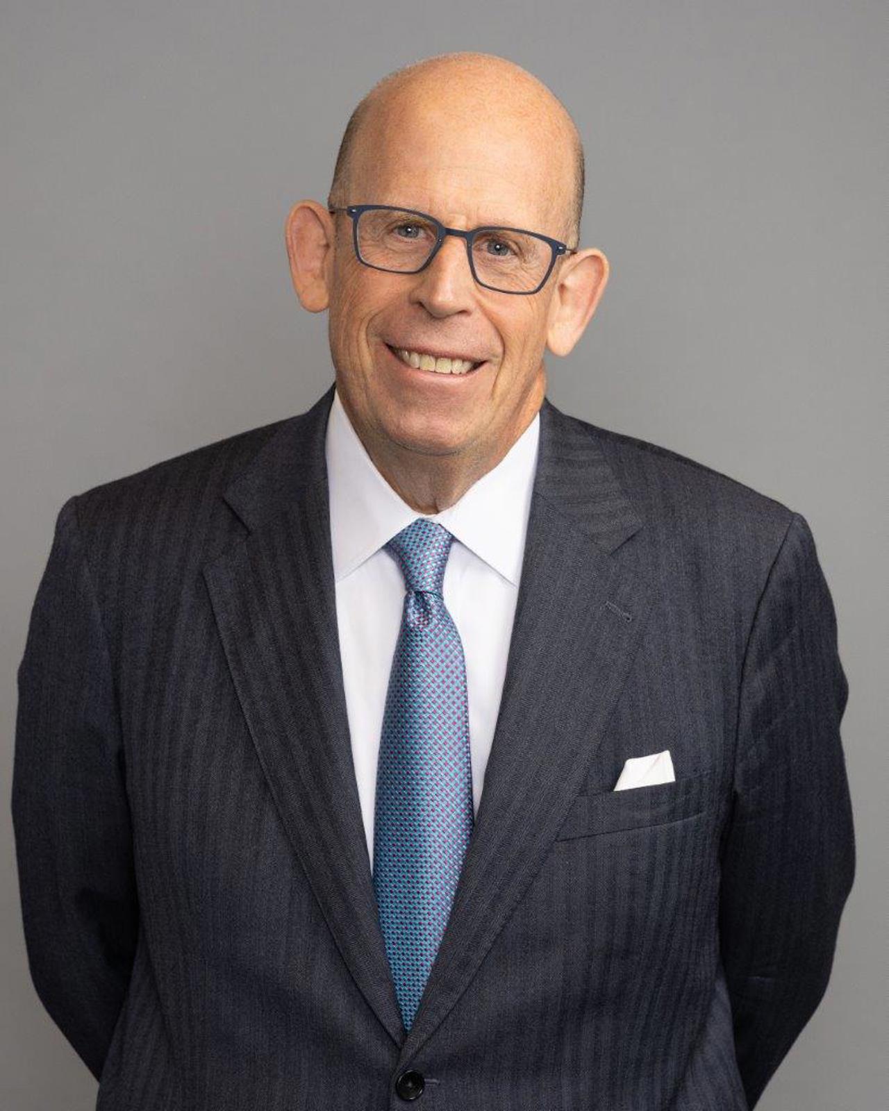 A headshot of Larry, wearing a black jacket and blue tie