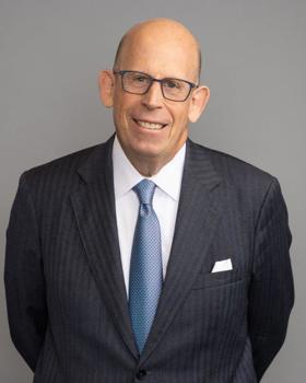 A headshot of Larry, wearing a black jacket and blue tie