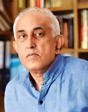 Portrait of Vir, bookcase behind him, looking into the camera. He is wearing a blue shirt.