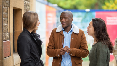 Three students standing and talking outside the Rhodes House building.