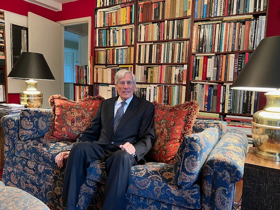 Richard wearing a suit sat on a sofa.