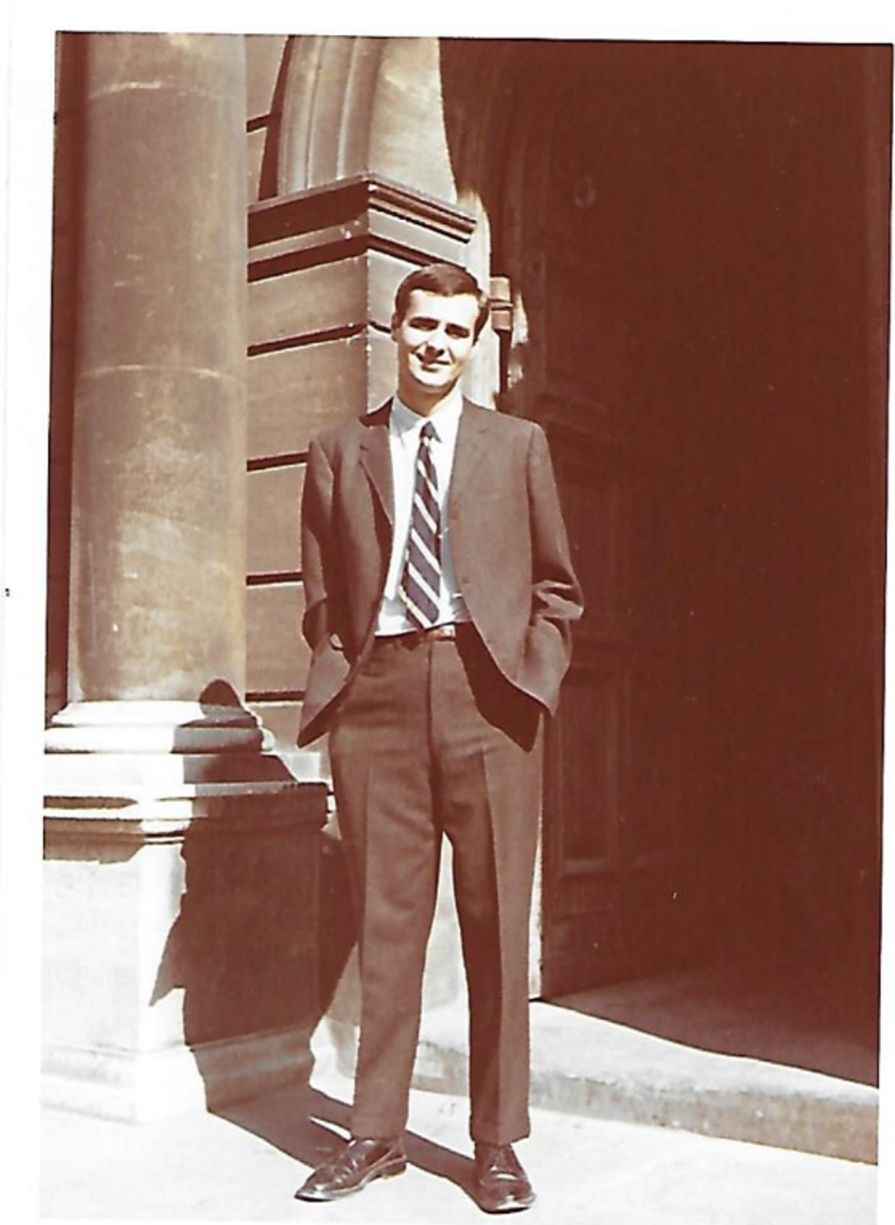 A sepia-tinted picture showing a young Jim in a suit standing in front of the main entrance to Hertford College