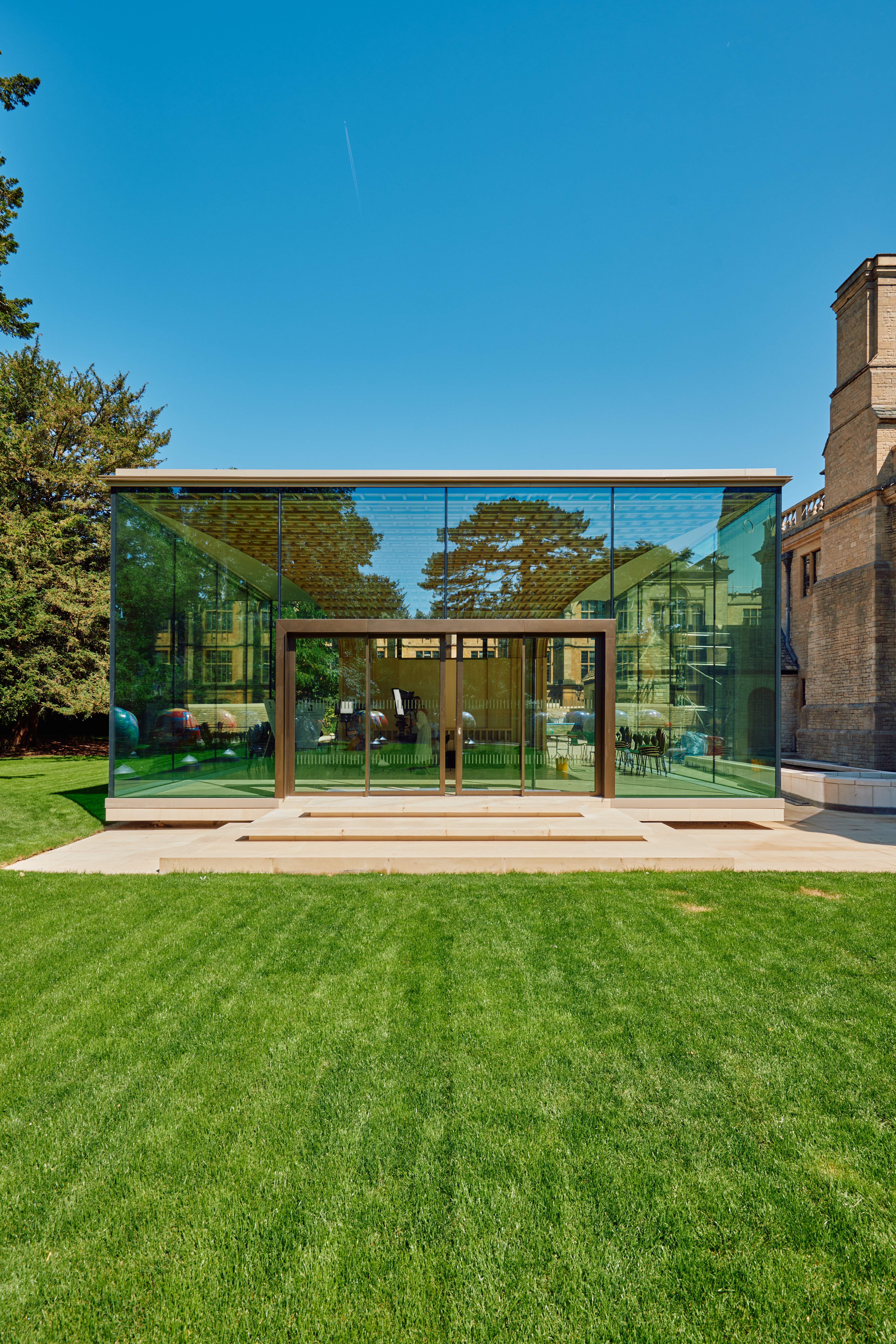 An image of the Rhodes garden pavilion from the outside. It has a glass front and sides, and is located on a lawn amongst some trees. 