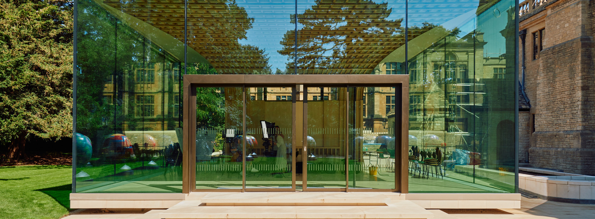 An image of the Rhodes garden pavilion from the outside. It has a glass front and sides, and is located on a lawn amongst some trees.