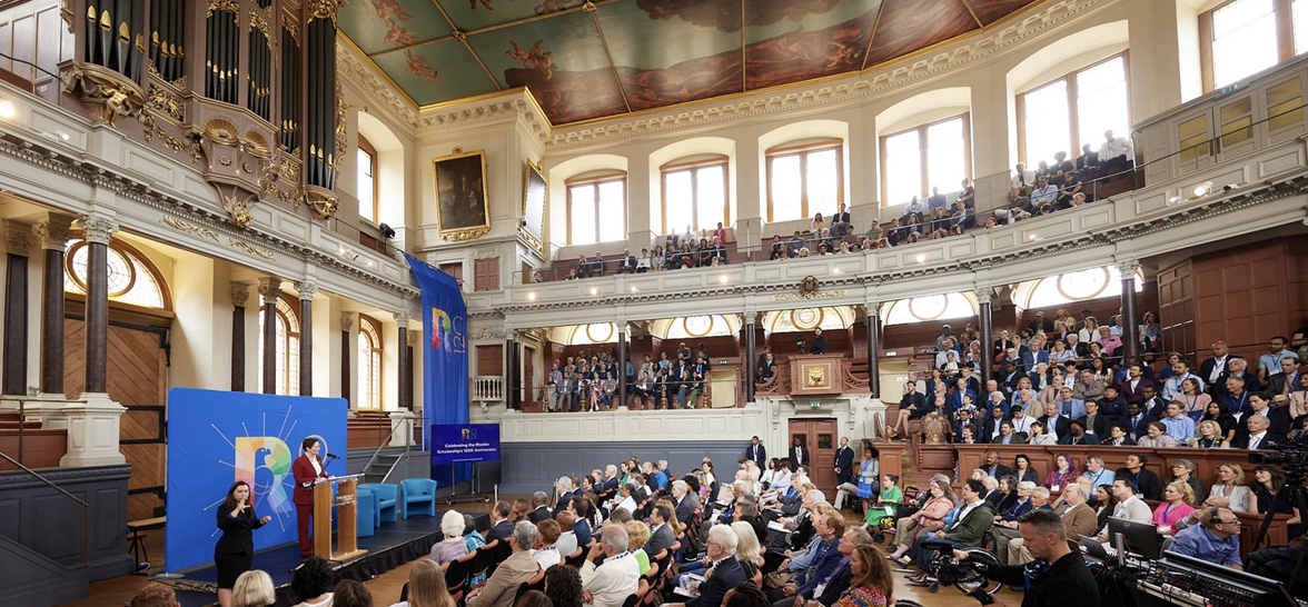 An image of more than 1300 Rhodes Scholars and friends gathered in a conference hall. The hall is a large historical building.