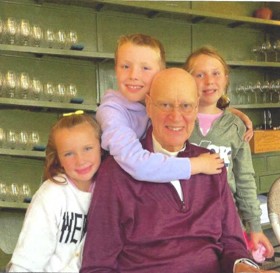 Willie sat in a burgundy jumper, and his three grandkids smiling around him. His grandson has his arm around him.