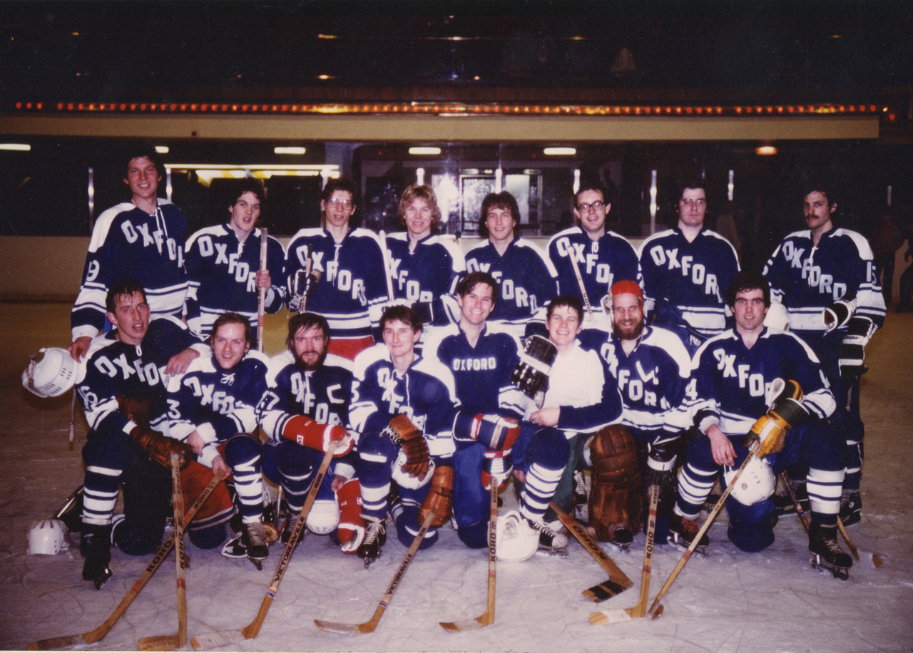 Photo of a hockey team assembled in tiers, all posing and holding their sticks out on the front-they are on an ice hockey pitch.