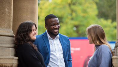 An image of three students standing and talking outside the Rhodes House building