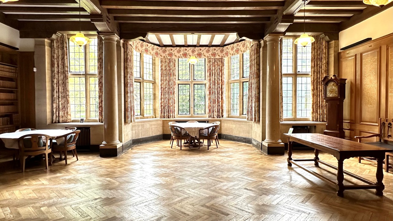 View of the Reception Room facing the bay window with a round table in the bay window and tables on the right and left sides of the room.