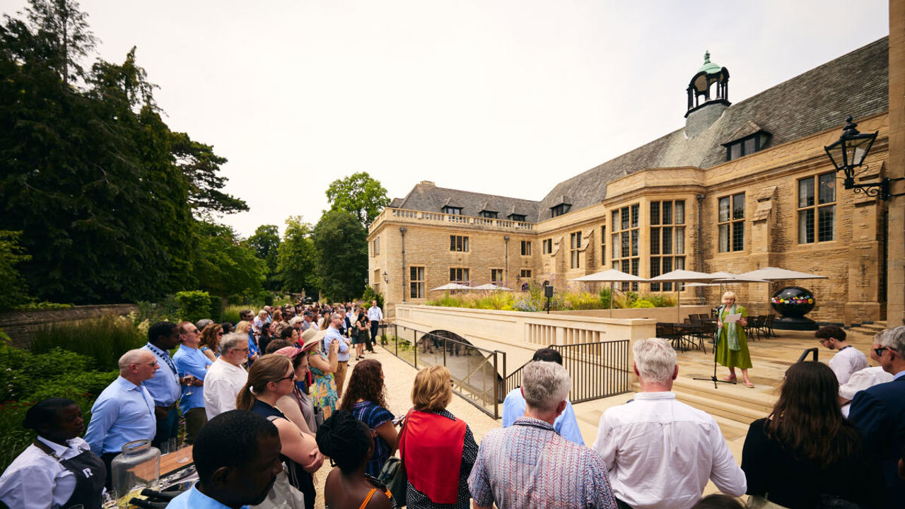 Professor Elleke Boehmer speaking to a crowd gathered in the Rhodes House gardens around the parapet inscription