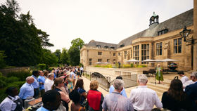 Professor Elleke Boehmer speaking to a crowd gathered in the Rhodes House gardens around the parapet inscription