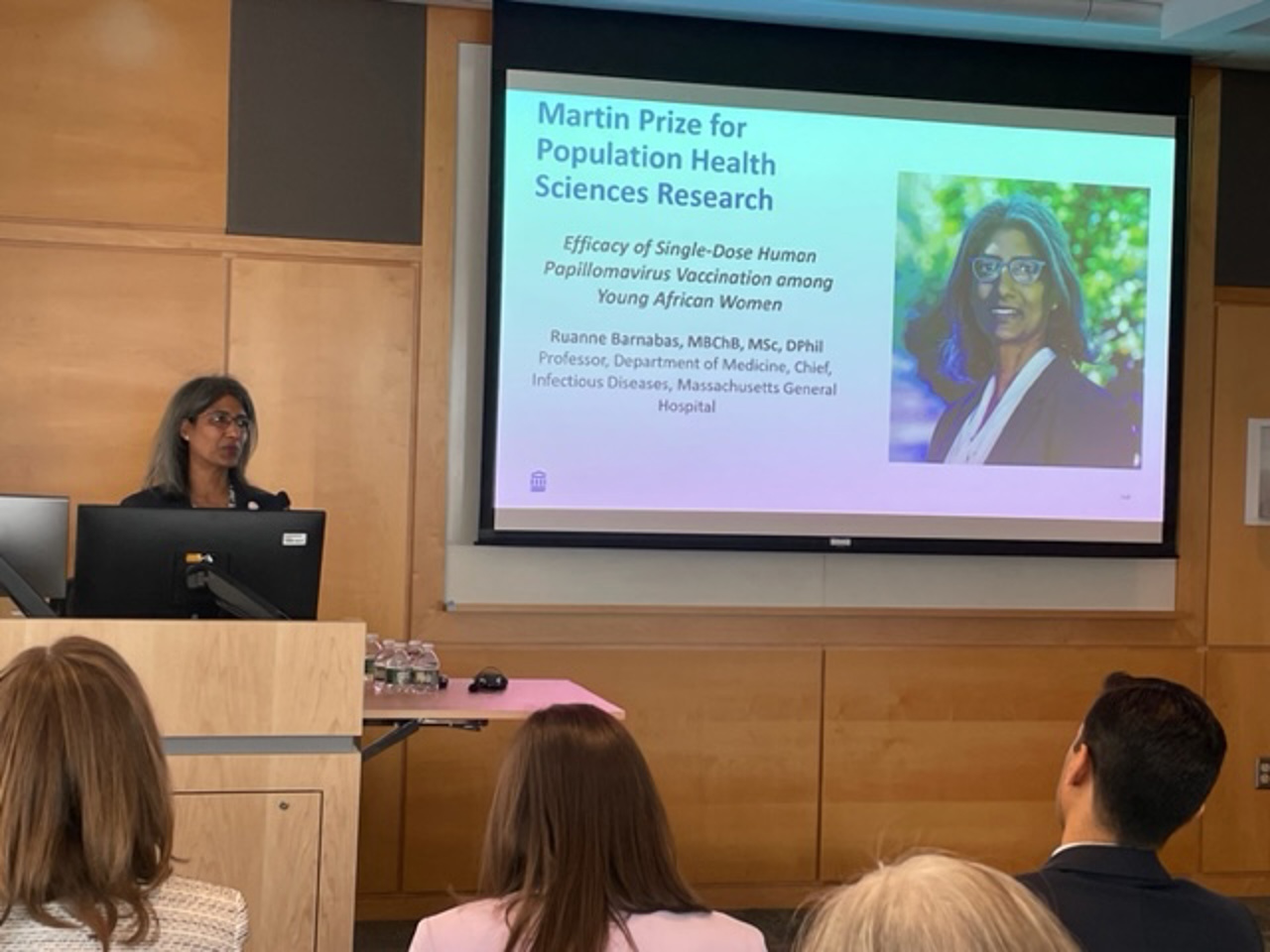 Ruanne stood at a podium with a powerpoint screen beside her, presenting to an audience.