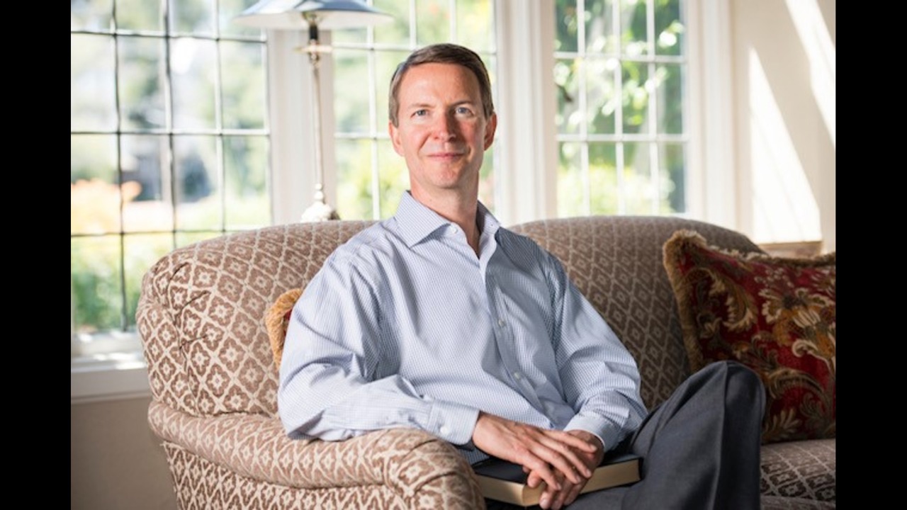 Bob seated on a sofa with glass windows in the background