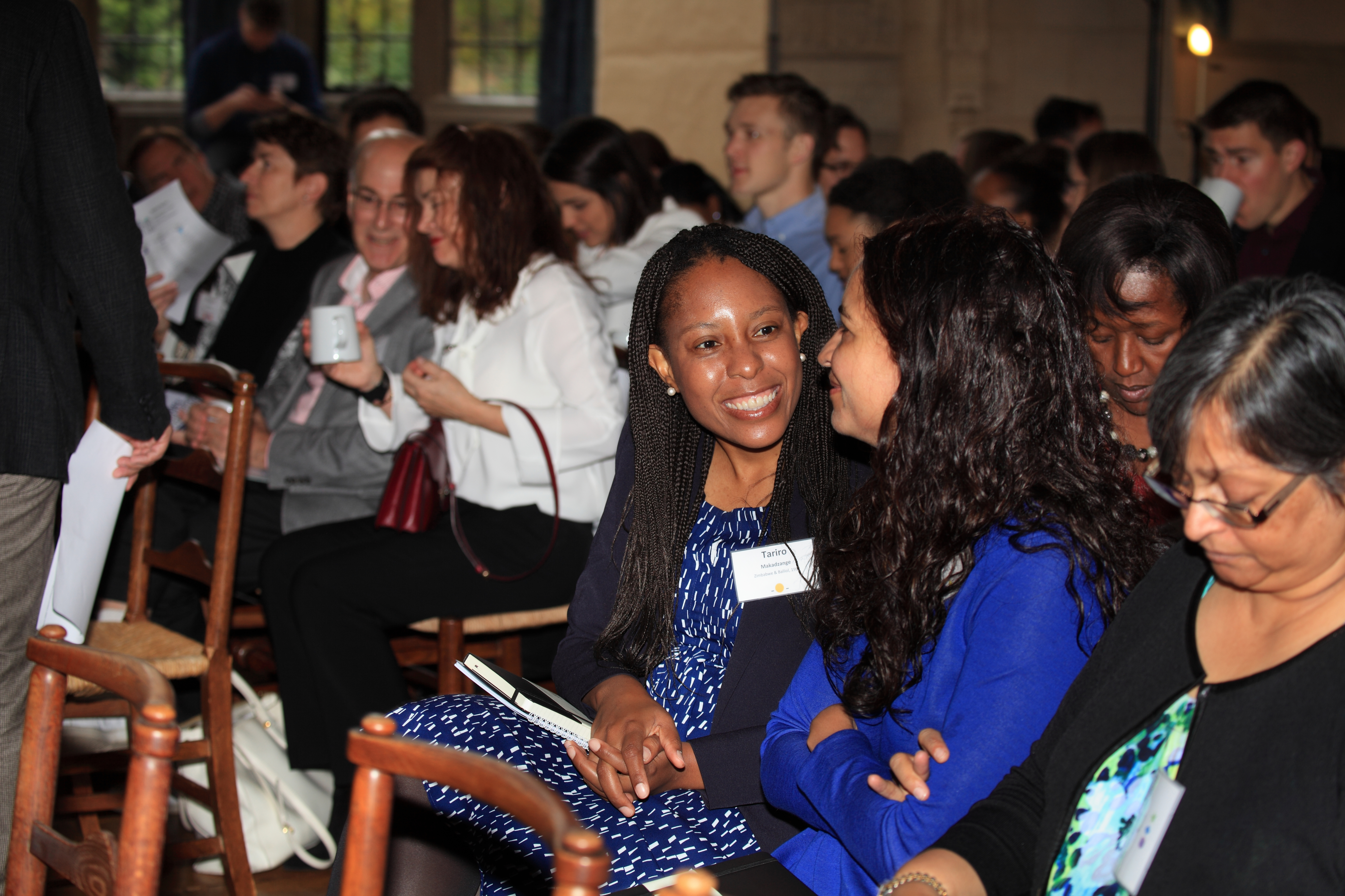 A picture of a crowd at a conference. In the foreground two women are talking and smiling. 