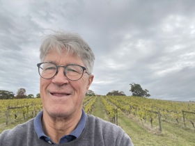 Mike taking a selfie smiling, wearing glasses. There is a farming field behind him.