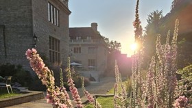 Flower border with Rhodes House and sunrise in the background.