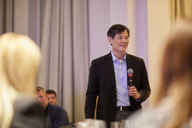The picture shows Philip in a dark suit with a light shirt, holding a microphone in his hand.