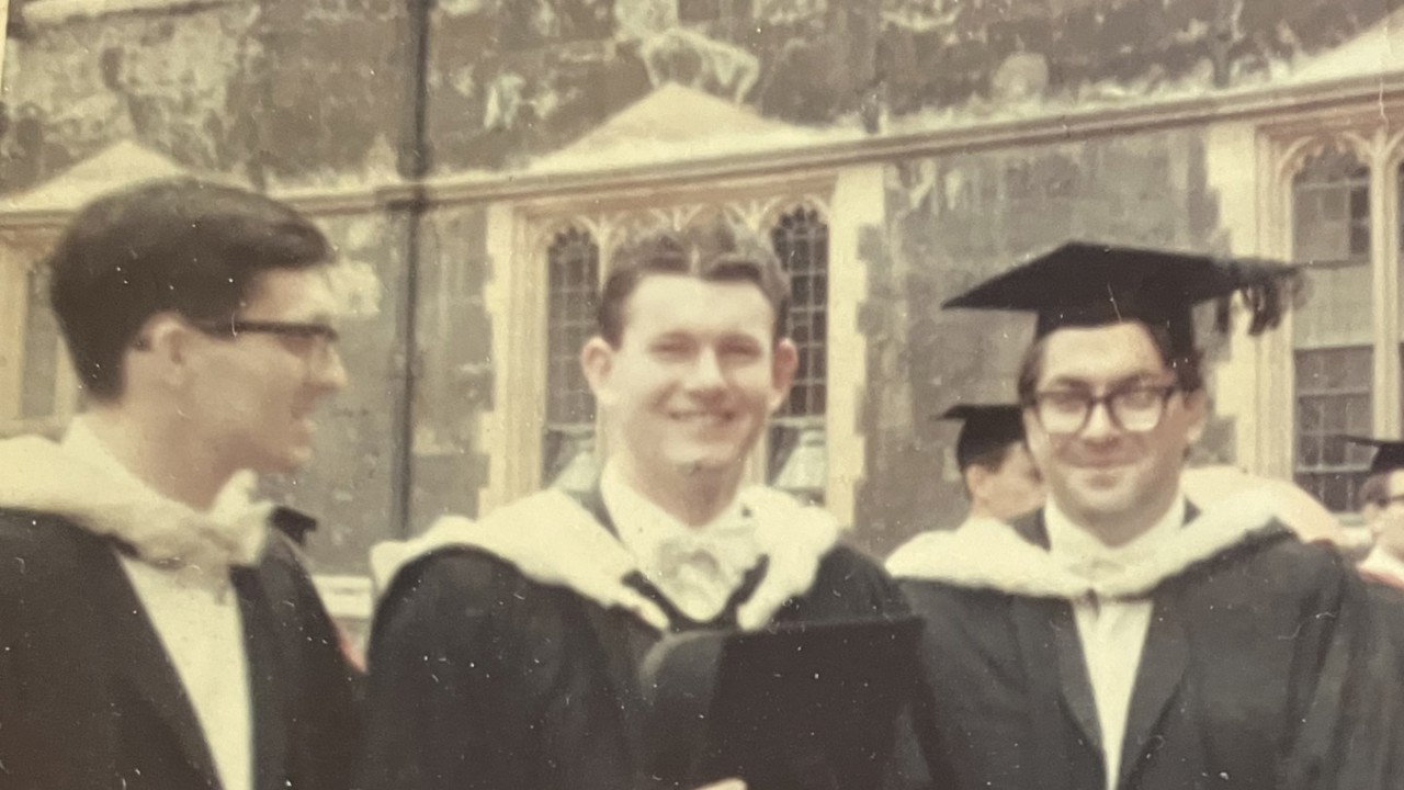 A black-and-white picture showing three men in graduation gowns. They are all smiling.
