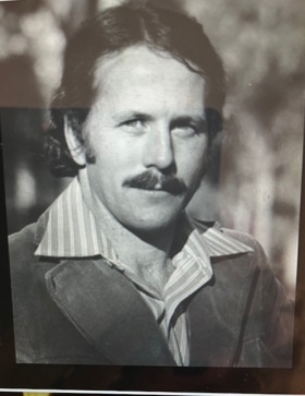 A black-and-white portrait of Peter. He's wearing a jacket over a striped shirt with large collars.
