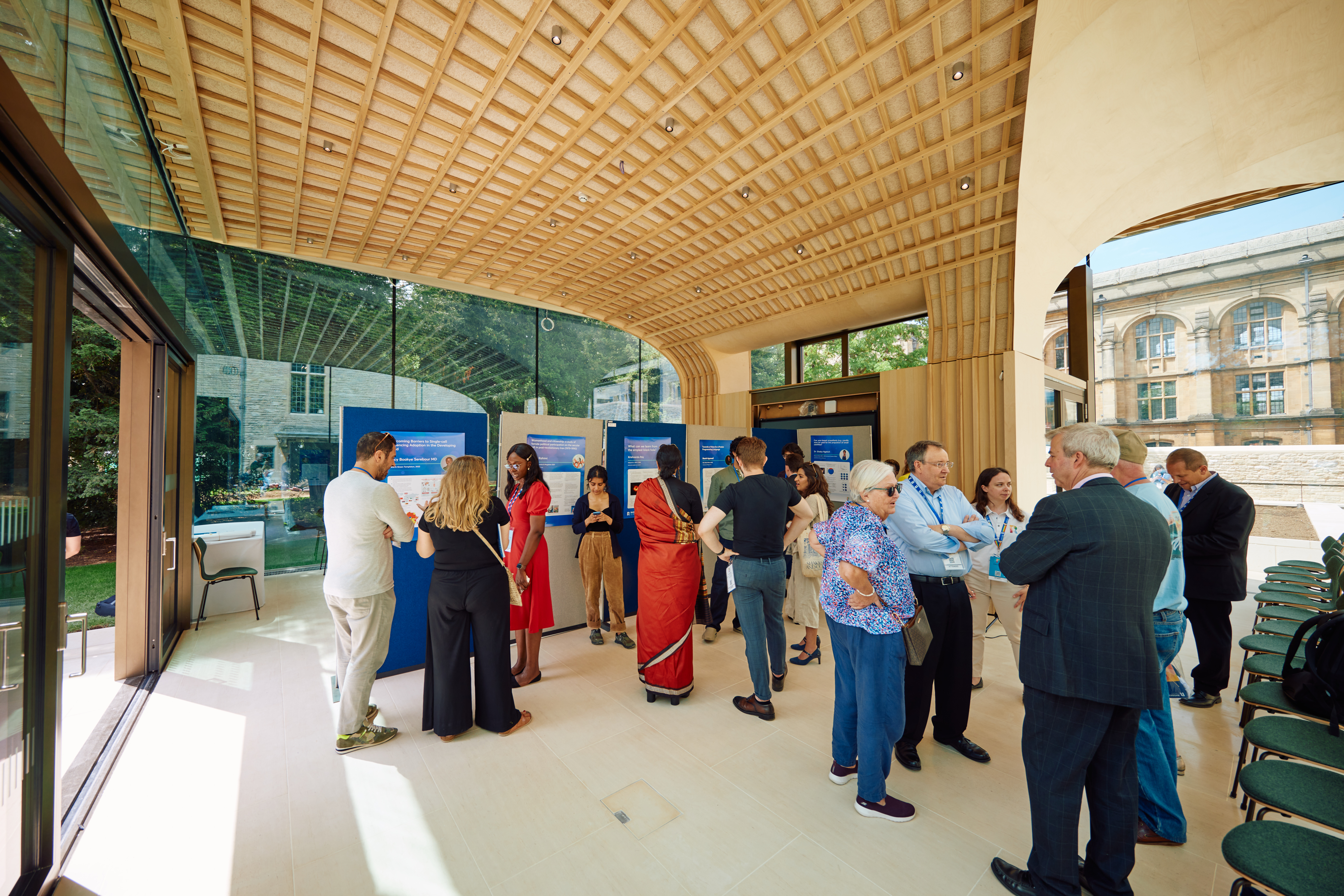 An image from the inside of the Rhodes Garden Pavilion. It is a wide room filled with people, with large glass doors and a modern-looking wooden ceiling. 