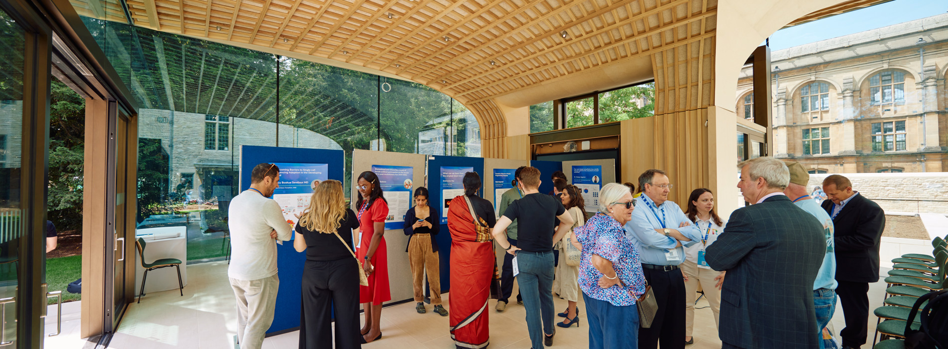 An image from the inside of the Rhodes Garden Pavilion. It is a wide room filled with people, with large glass doors and a modern-looking wooden ceiling.
