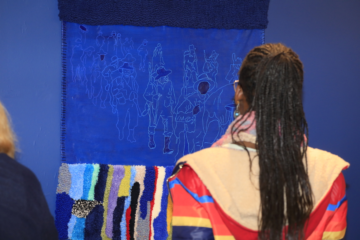 A visitor gazing at a blue artwork with colourful tufted material.