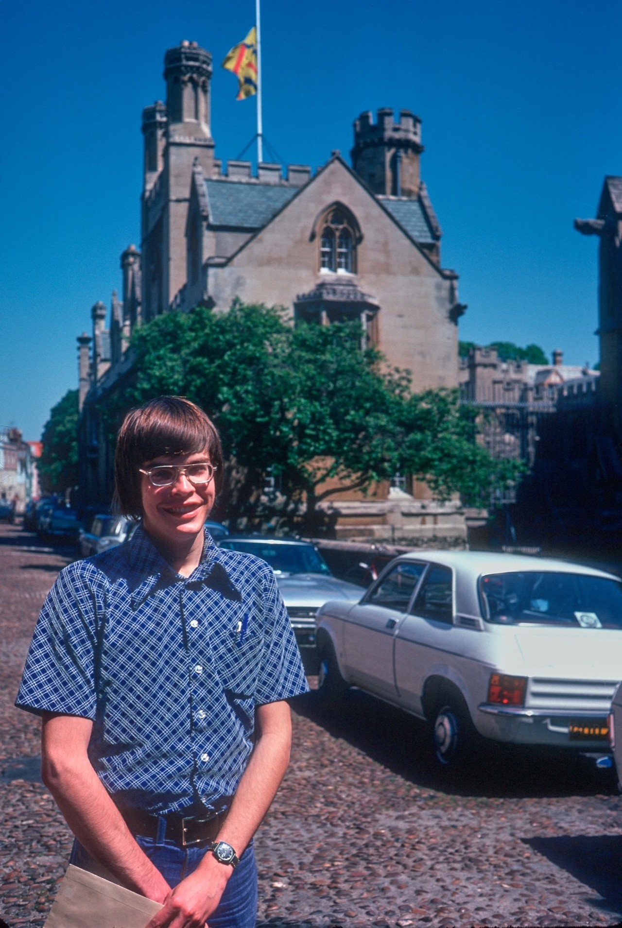 Rob as a young man in Oxford stood smiling on a street, blue sky in the background.
