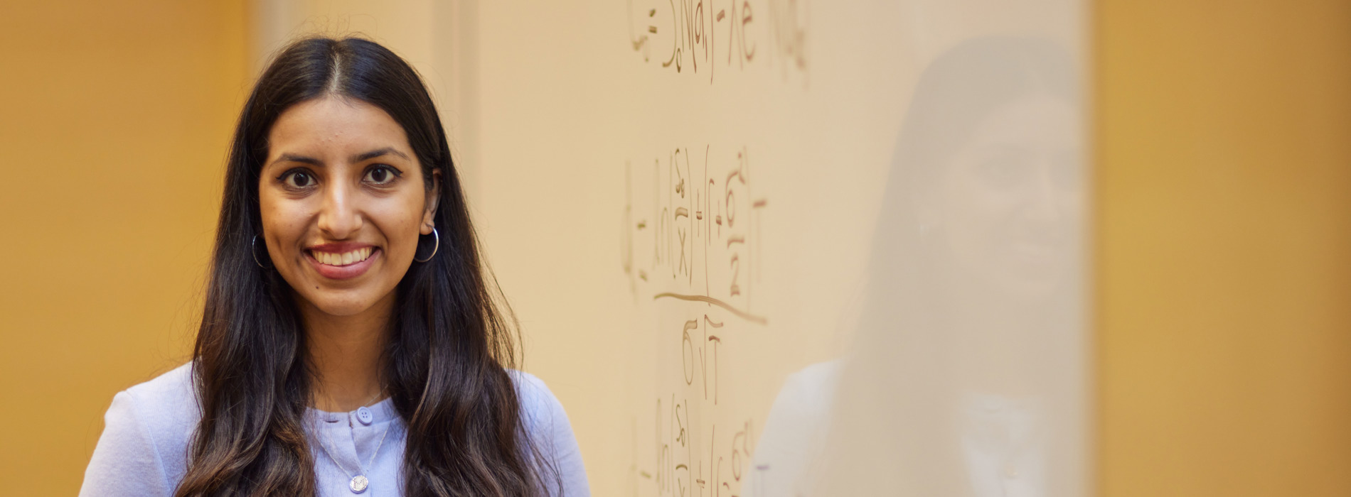 A woman Scholar smiling at the camera in front of a whiteboard with mathematical calculations