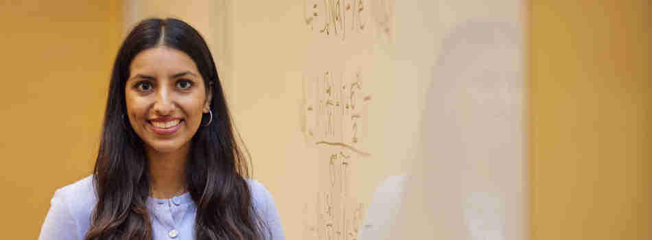 A woman Scholar smiling at the camera in front of a whiteboard with mathematical calculations